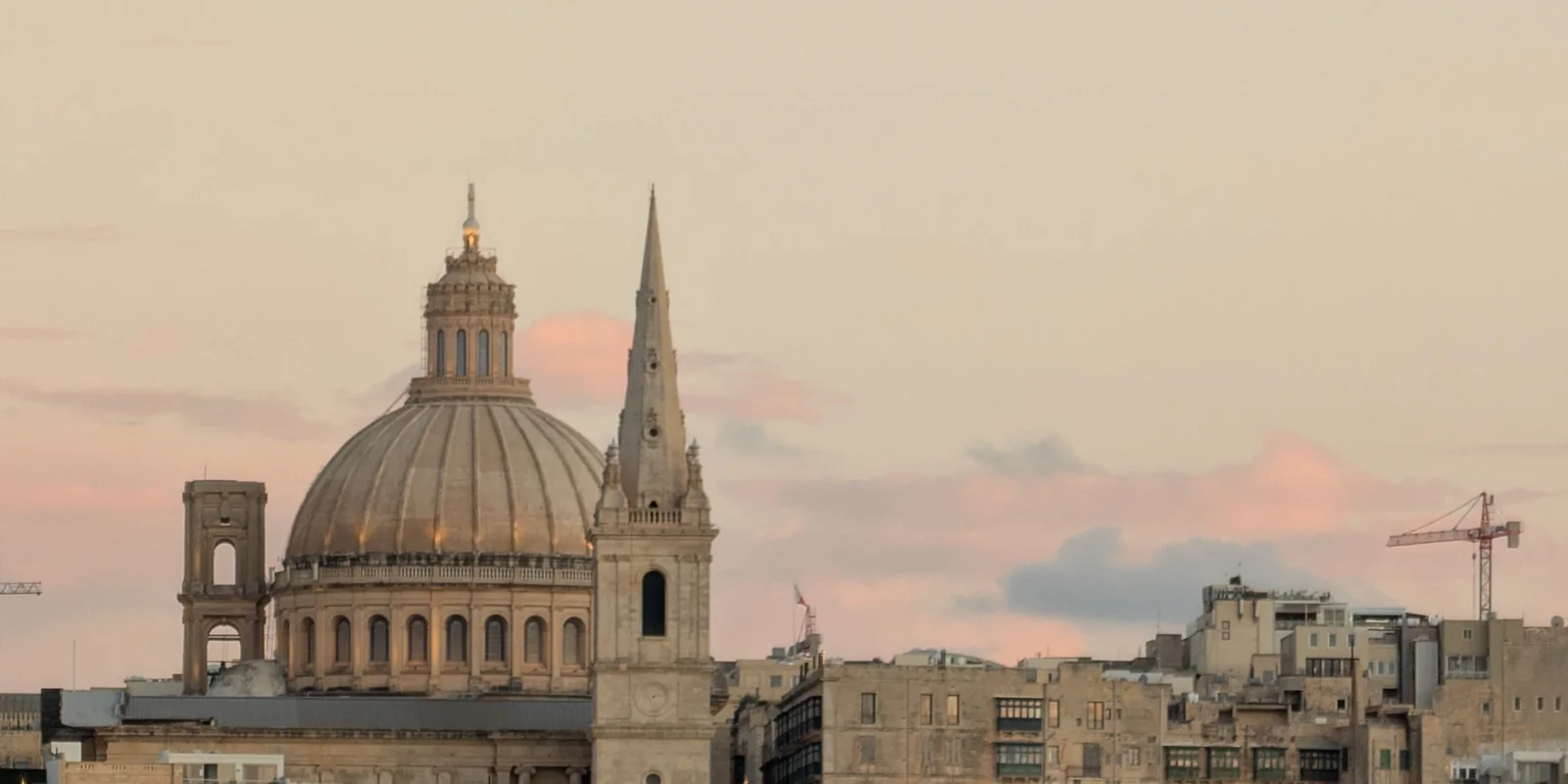 The dome of the Carmelite Church and St Paul's Cathedral spire above Valletta at dusk, seen from a boat on the water
