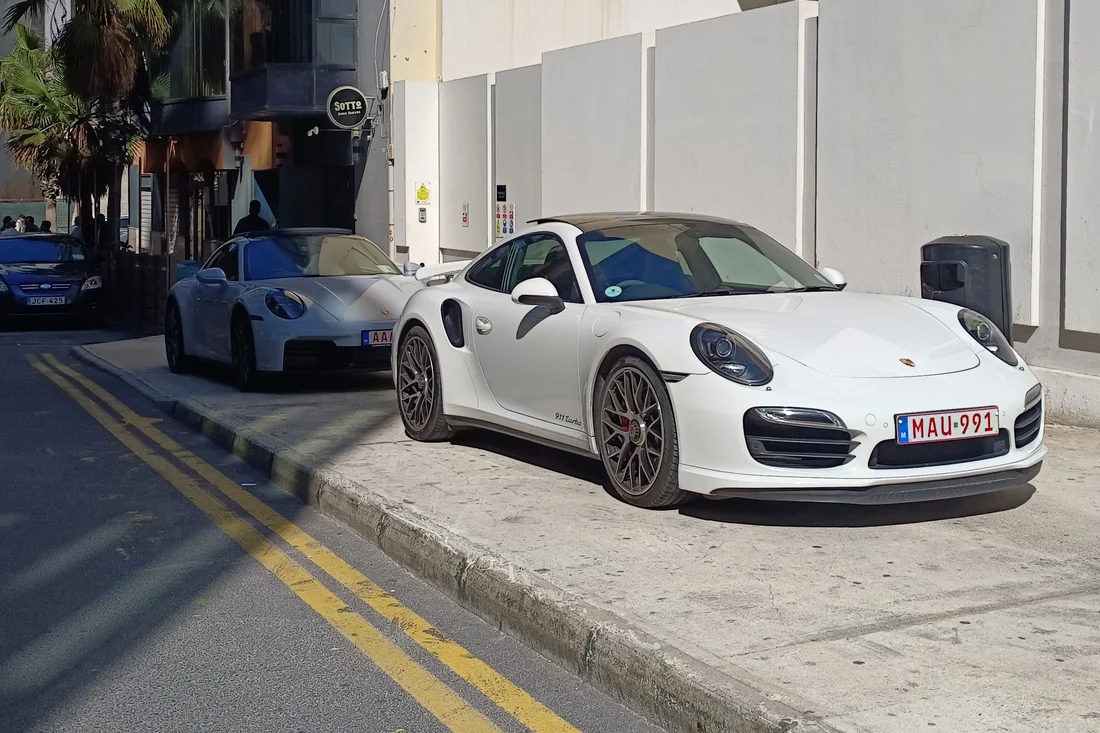 Two Porsche 911 Turbos parked nose to tail on a kerb marked with double yellow lines in Malta